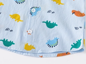 Vue macro d'une chemise enfant bleue en coton avec dinosaures colorés et boutons blancs