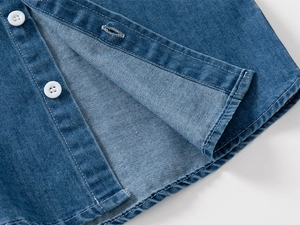 Dettaglio della camicia di jeans blu classica con bottoni bianchi e cuciture sull'orlo