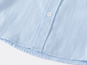Close-up of light blue cotton shirt featuring white resin buttons and twill fabric texture
