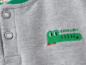Detailed macro view of gray knit fabric with green crocodile embroidery on kids' sweater