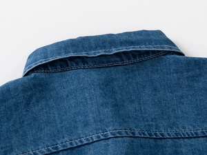 Dettaglio macro del colletto della camicia di jeans blu con cuciture a contrasto e twill