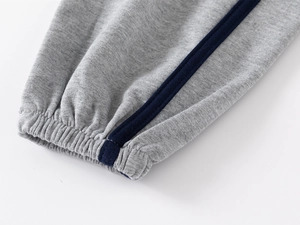 Macro view of grey kids joggers showing elastic ribbed cuffs and navy side stripes detail
