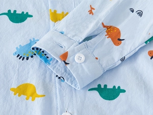 Gros plan de la manche d'une chemise enfant bleu clair avec motifs dinosaures et bouton blanc