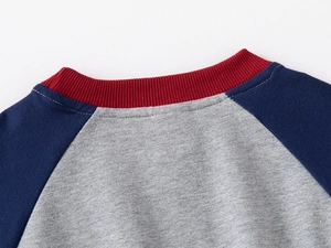 Close-up of raglan neckline with red ribbing and navy sleeves on a grey cotton sweater