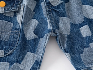 Detail of patched denim shorts with orange button accent and contrast stitching