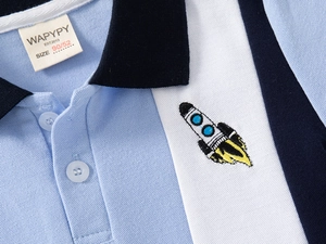 Close-up of children's blue polo shirt with cartoon rocket embroidery and color block detail