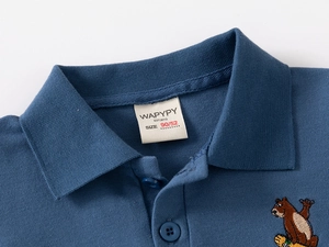 Détail du col d'un polo bleu avec broderie ours et étiquette de taille blanche