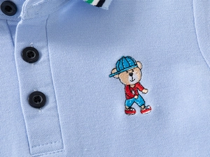 Detail of light blue boys polo shirt with embroidered bear and textured pique fabric