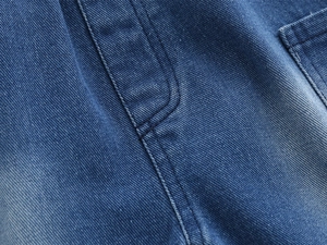 Detailed macro view of denim fabric with visible twill weave and double-stitch sewing seams