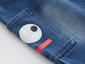Detail of blue denim shorts featuring a cartoon eye print and red line on the side pocket