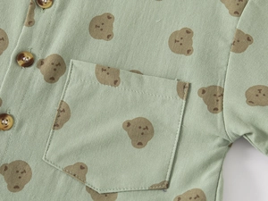 Detail of baby shirt with bear print, chest pocket and resin buttons on green fabric