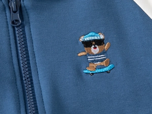 Dettaglio del ricamo a forma di orso e cerniera sulla giacca blu scuro da bambino