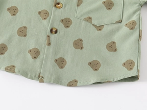 Detailed close-up of bean green cotton shirt with brown cartoon bear print and pocket