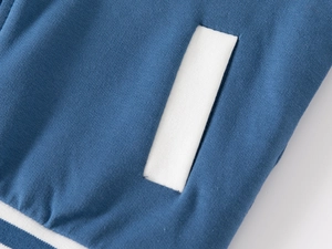 Dettaglio giacca baseball blu con tasca a contrasto bianca e bordo a coste rigate