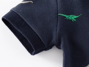 Détail macro d'un polo enfant montrant la broderie dinosaure et la texture du poignet
