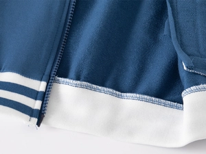 Dettaglio giacca baseball blu con cerniera e orlo a righe bianche in tessuto French Terry