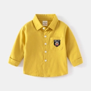 Detail of ginger yellow cotton shirt featuring a bear embroidery pocket and white buttons