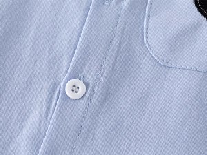 Close-up of light blue cotton fabric with white buttons on boys long sleeve shirt