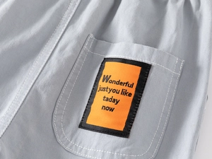 Détail de la poche arrière du short en coton gris avec une étiquette brodée orange vif