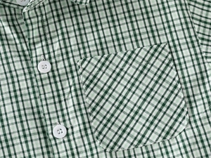 Detail showing the green plaid shirt with a bias-cut chest pocket and white resin buttons