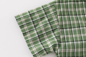 Detailed view of the green plaid cotton fabric and high-quality stitching on child shirt