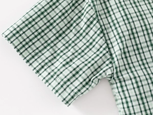 Detailed close-up of neat stitching on the cuff of a green plaid cotton shirt for kids