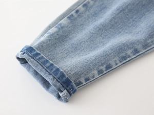 Detail of light blue denim cuff showing washed texture and twill stitching on boy's jeans