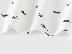 Macro shot of soft white knit fabric with dark green dinosaur patterns for kids