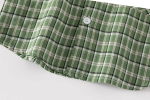 Detailed view of the green plaid shirt hem with white button and precise stitching