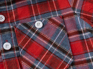 Détail d'une chemise en coton à carreaux rouges avec poche poitrine et bouton blanc