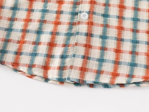 Detail of classic orange and blue plaid shirt featuring white buttons and curved hem stitching
