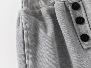 Detail der grauen Baby-Strickhose mit drei dekorativen schwarzen Knöpfen und Seitentaschen