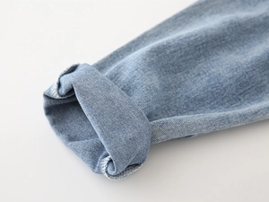 Detail of light blue denim cuff with rolled edge showing stitching and twill texture