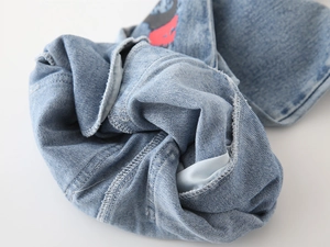 Detailed macro view of denim fabric with red printed patterns and stitching on kids jeans