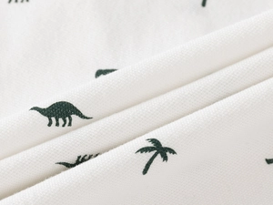 Macro detail of breathable cotton fabric with green dinosaur and palm tree print