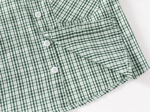 Detailed view of green plaid fabric with white buttons and pocket on kids shirt