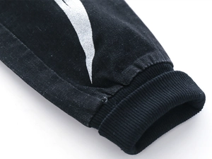 Detailed macro view of black ribbed cuffs and silver metallic wing print on denim pants