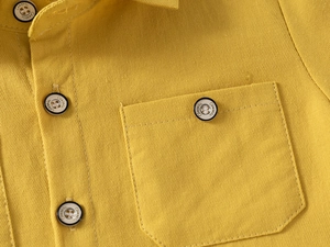 Close-up of yellow cotton shirt collar with black button and chest pocket detail