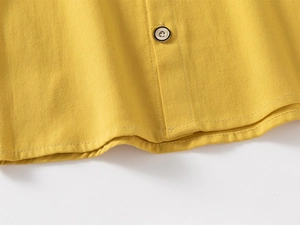 Detailed macro view of a yellow cotton shirt showing a classic black round button