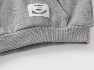 Close-up of gray knitted hoodie showing ribbed hem and stitched fabric brand label
