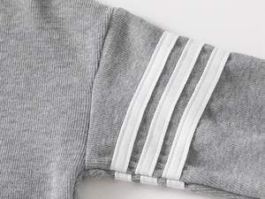 Detail of grey kid's hoodie sleeve with signature white four-stripe sporty pattern