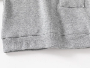 Detailed close-up of grey knit sweatshirt fabric texture with ribbed hem and square pocket