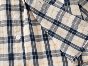 Dettaglio di camicia a quadri per bambini con bottoni bianchi e cuciture polsini rifinite
