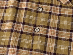 Detailed macro view of mustard yellow plaid flannel fabric and classic engraved buttons