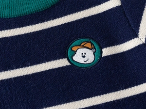 Detailed close-up of striped knit sweater showing green ribbed collar and cartoon embroidery