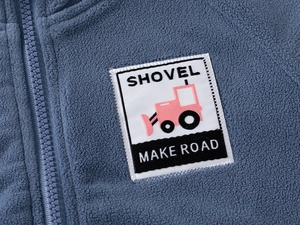 Détail de la veste en polaire bleue montrant la fermeture éclair et le patch brodé