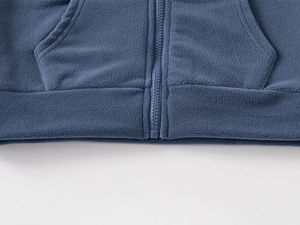 Détail de veste polaire enfant montrant la fermeture éclair, poches et ourlet côtelé