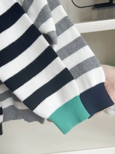 Detailed close-up of striped knit sweater with asymmetrical green and black cuffs
