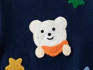 Detail shot of navy knit vest featuring premium teddy bear embroidery and star accents
