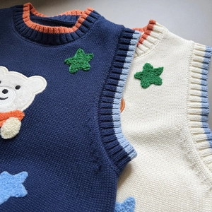 Detailed view of knitted kids vests with cute teddy bear embroidery and ribbed trims